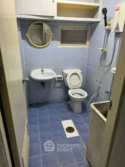 Compact bathroom with blue tiles, wall-mounted sink, and shower area.