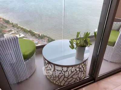 Stunning balcony with ocean view, stylish furniture, and glass railing in luxury high-rise apartment.