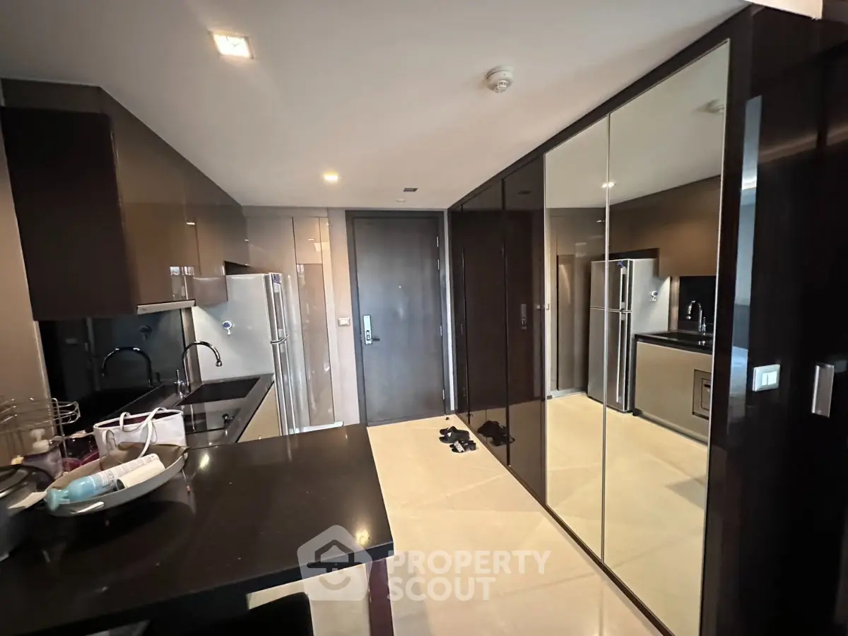Modern kitchen with sleek black cabinetry and mirrored walls, featuring stainless steel appliances and elegant design.