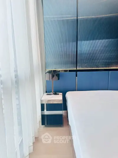 Modern bedroom with sleek design, featuring a stylish bed and contemporary side table by large windows.