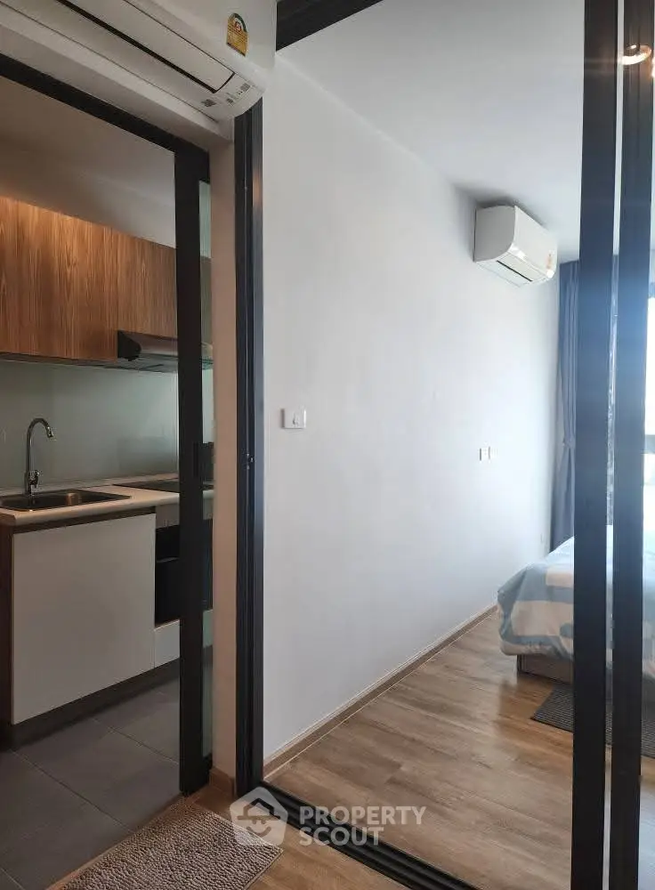 Modern apartment interior with sleek kitchen and cozy bedroom, featuring air conditioning and wooden flooring.