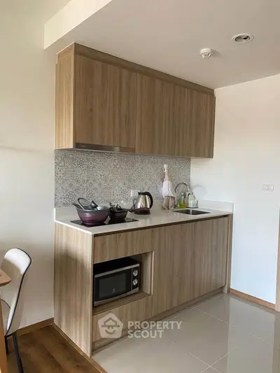 Modern kitchen with wooden cabinets, microwave, and sleek countertop in a cozy apartment.