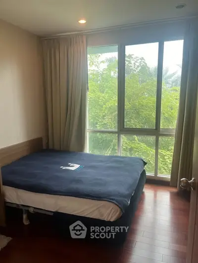 Cozy bedroom with large window and lush greenery view, perfect for relaxation.