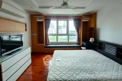 Spacious bedroom with large window and modern furnishings in urban apartment.