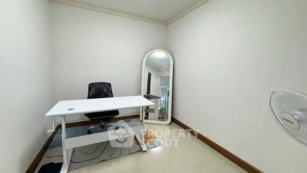 Minimalist home office with white desk, black chair, and large mirror in a bright room.