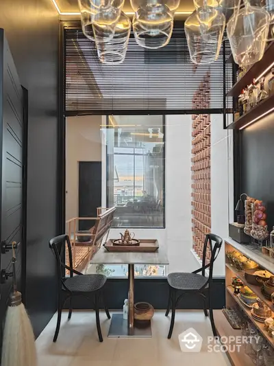 Chic urban kitchenette with modern design, featuring unique overhead glass storage, sleek surfaces, and a cozy dining nook with a view.