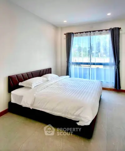 Spacious bedroom with large window and elegant curtains in modern apartment.