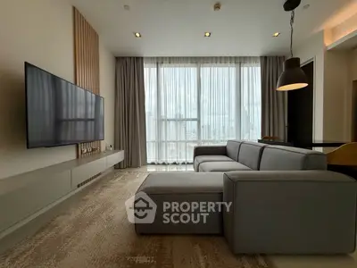 Modern living room with large TV and stylish gray sofa, featuring floor-to-ceiling windows with city view.