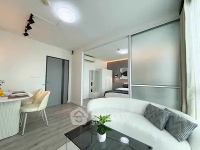 Modern open-plan living room with dining area and sliding doors to bedroom, featuring sleek furniture and decor.