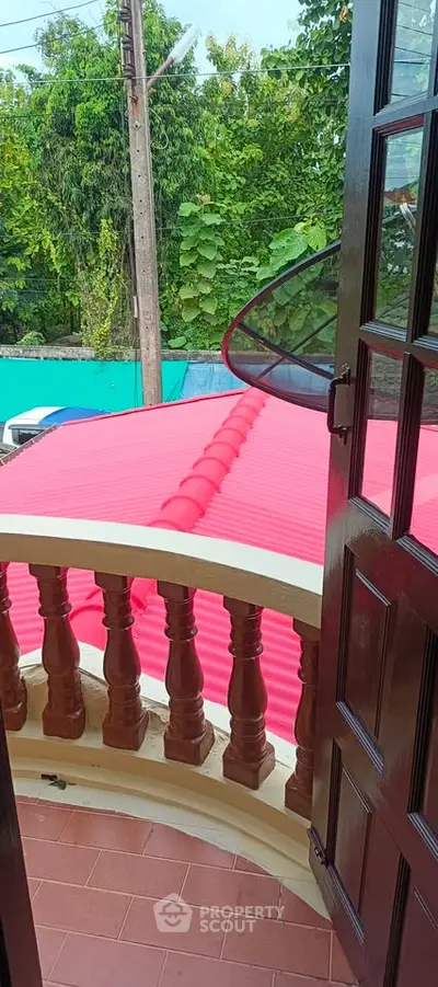 Charming balcony view with vibrant red roof and lush greenery, perfect for serene outdoor relaxation.