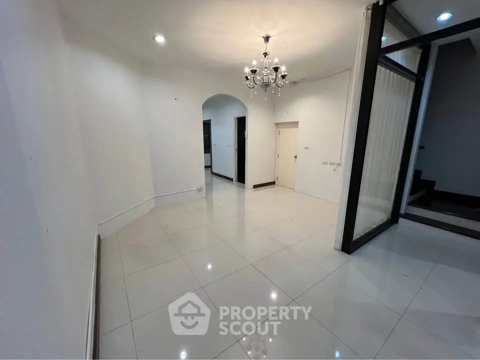 Spacious modern living room with elegant chandelier and glossy tiled flooring.