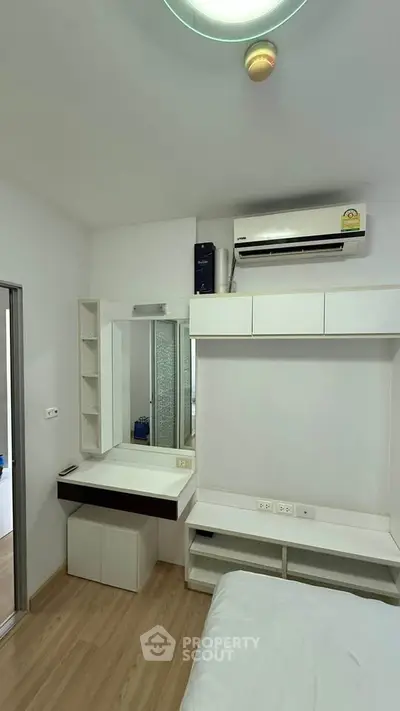 Modern bedroom with built-in storage and air conditioning, featuring sleek white furniture and wood flooring.
