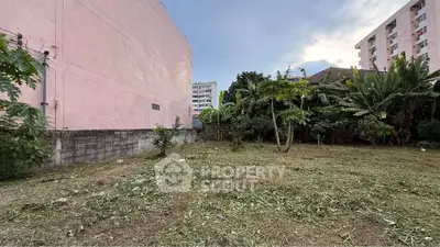 Spacious urban land plot with potential for development, surrounded by greenery and city buildings.