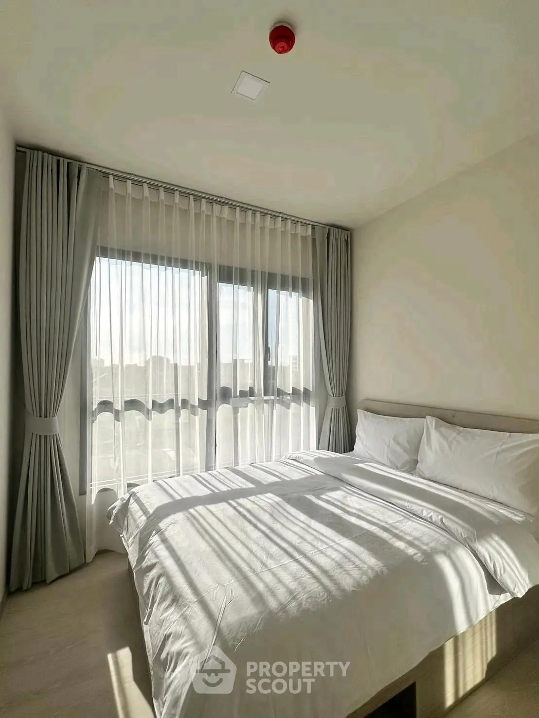 Bright and cozy bedroom with large window and elegant curtains, perfect for relaxation.