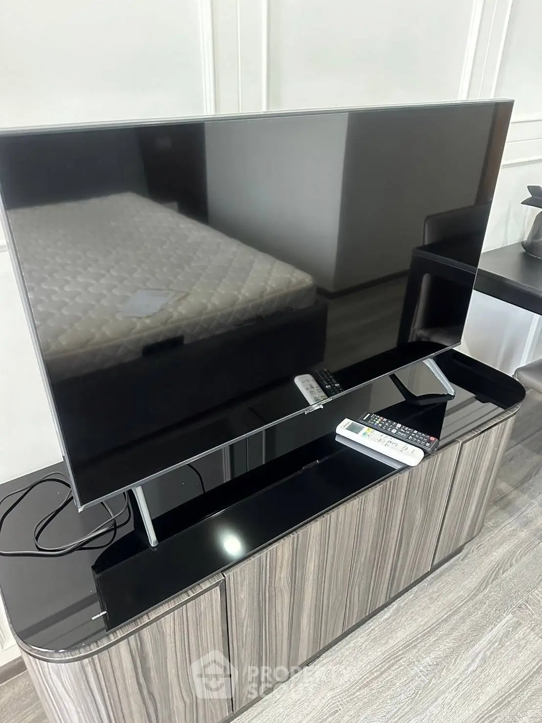 Modern living room with sleek TV stand and large flat-screen TV, adjacent to a comfortable bed.