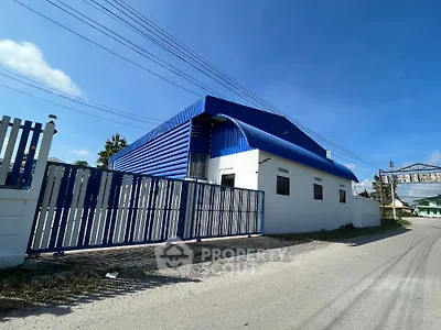 Industrial warehouse with blue roof and secure gated entrance on sunny day