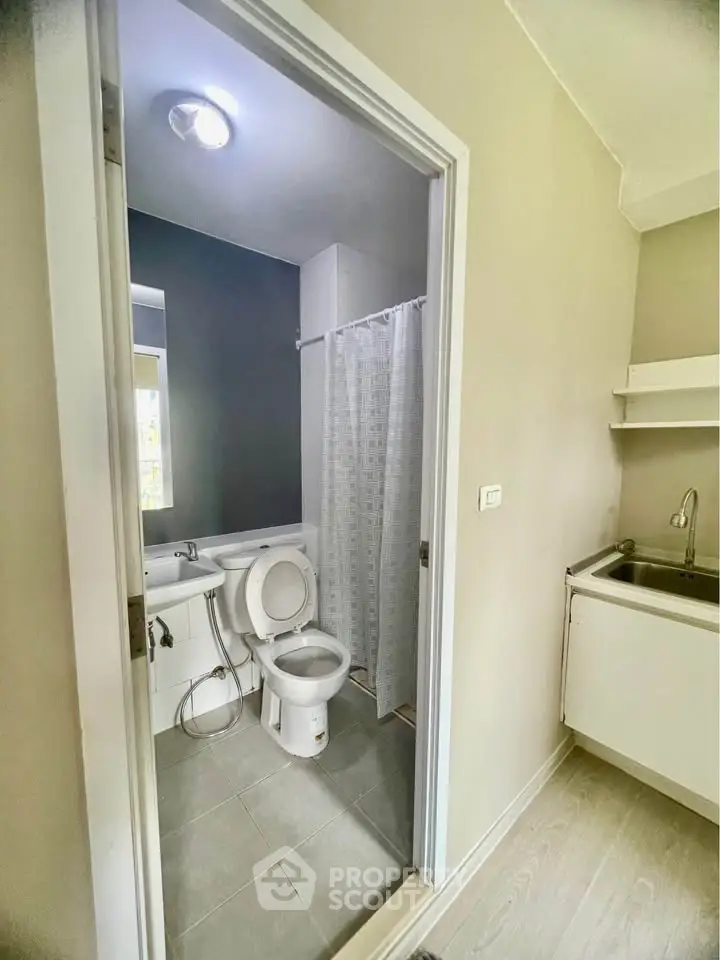 Compact bathroom with modern fixtures and adjacent kitchenette in cozy apartment.