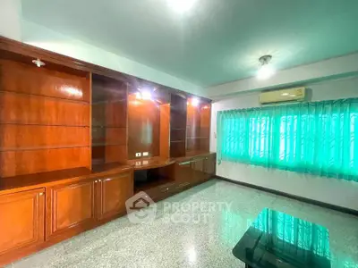 Spacious living room with built-in wooden shelves and large window with green curtains.