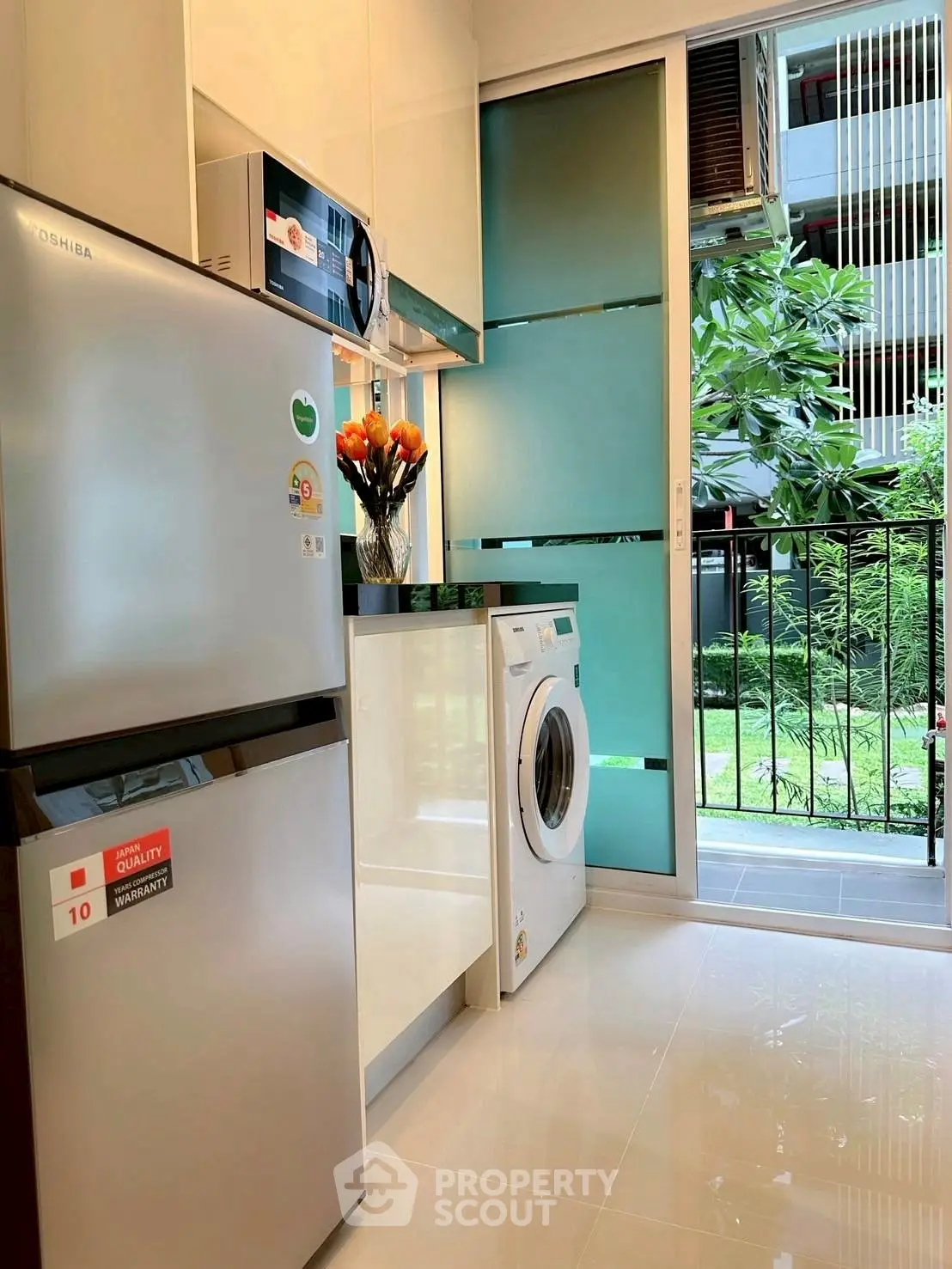 Modern kitchen with stainless steel appliances and garden view, featuring a washing machine and sleek design.