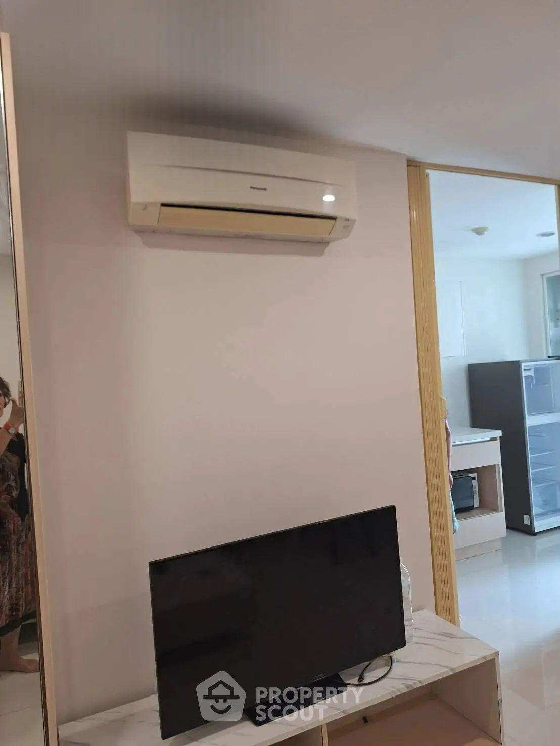 Modern living room with air conditioning and TV setup, featuring sleek furniture and a glimpse of the kitchen area.