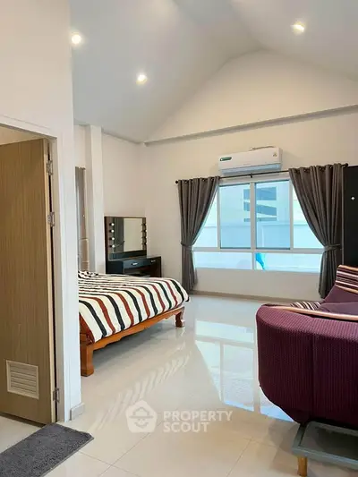 Spacious bedroom with modern decor and large window offering natural light.