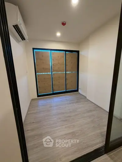 Compact room with wooden flooring and large window, ideal for a cozy study or small bedroom.