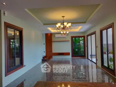 Spacious living room with elegant chandelier and large windows overlooking lush greenery.