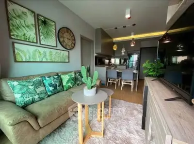 Stylish living room with modern decor and open kitchen layout, featuring lush green accents and cozy seating.