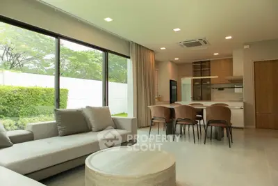 Spacious modern living room with open kitchen and garden view, featuring elegant furniture and large windows.