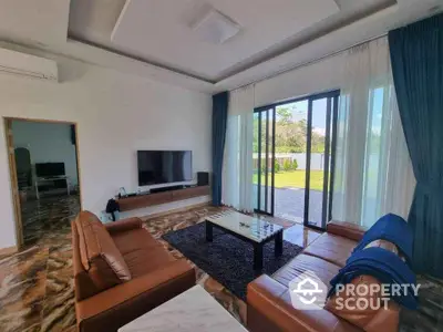 Spacious modern living room with leather sofas and large glass doors opening to garden view.