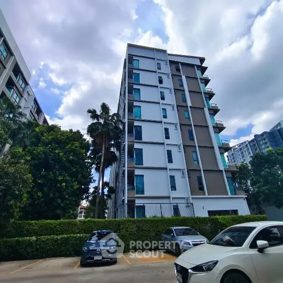 Modern apartment building with lush greenery and parked cars in urban setting.