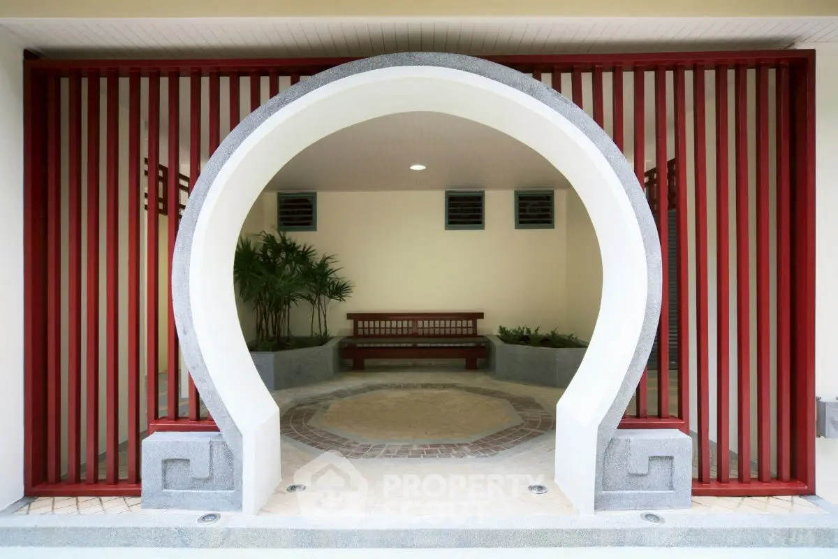 Elegant entrance with unique archway and red accents, inviting seating area, and lush greenery.