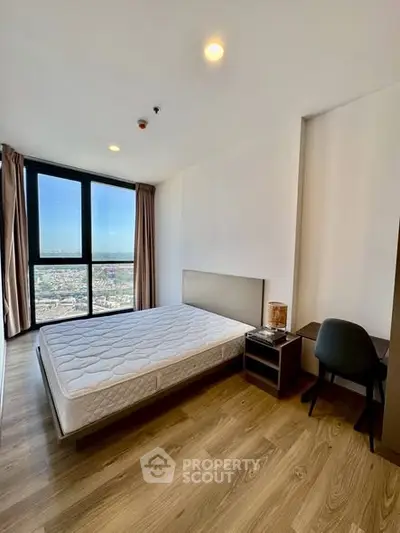 Modern bedroom with large window offering stunning city view, featuring wooden flooring and minimalist furniture.