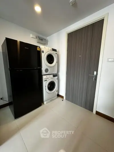 Modern laundry area with stacked washer and dryer next to a sleek black refrigerator.