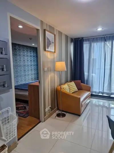 Modern living room with cozy seating and stylish decor, adjacent to a chic bedroom with patterned wallpaper.