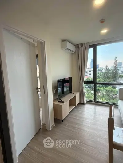 Modern living room with large window and city view, featuring sleek furniture and air conditioning.