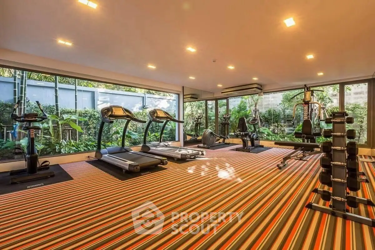 Spacious modern gym with large windows and lush garden views, featuring state-of-the-art fitness equipment.