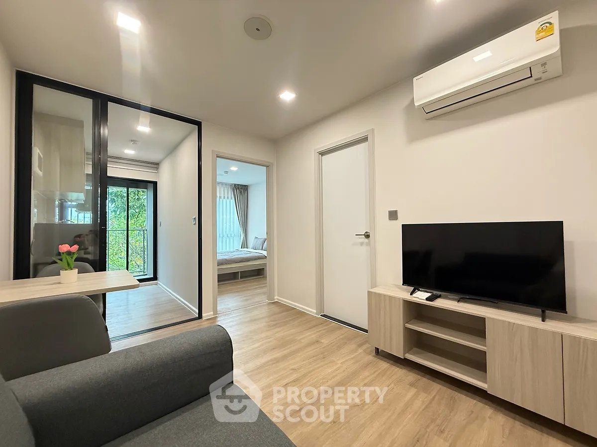 Modern living room with sleek design, featuring a cozy sofa, flat-screen TV, and air conditioning, leading to a bedroom.