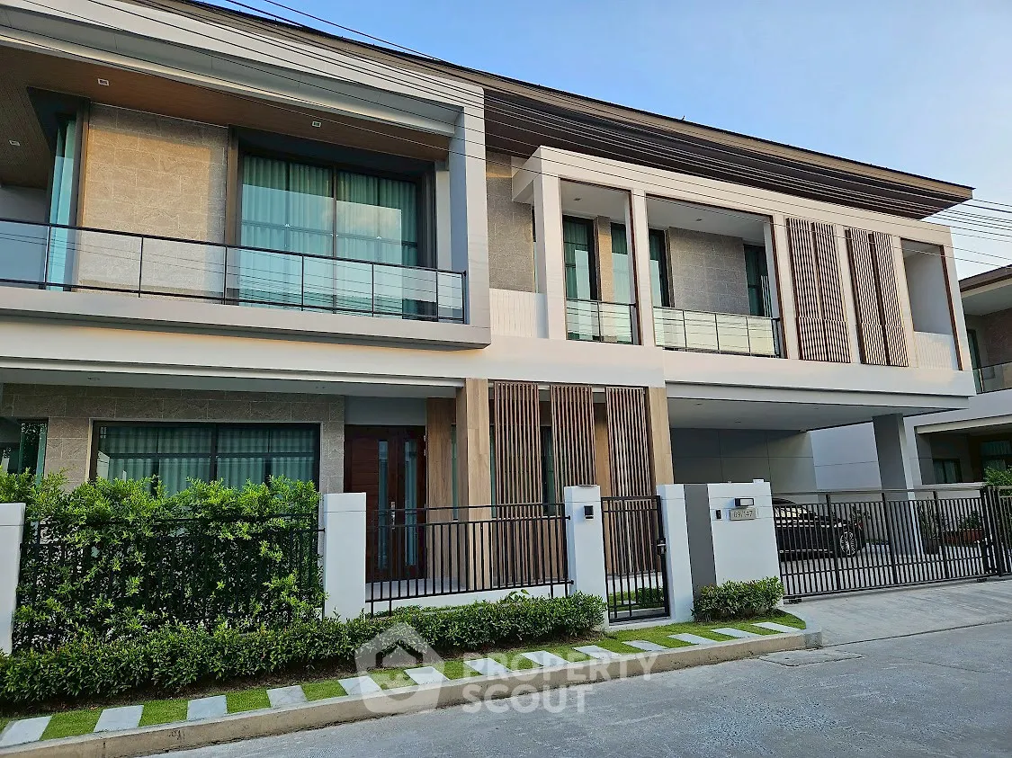 Modern two-story house with sleek design and large windows, featuring a well-maintained front garden.