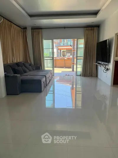 Spacious living room with modern sofa and large TV, featuring floor-to-ceiling windows for natural light.