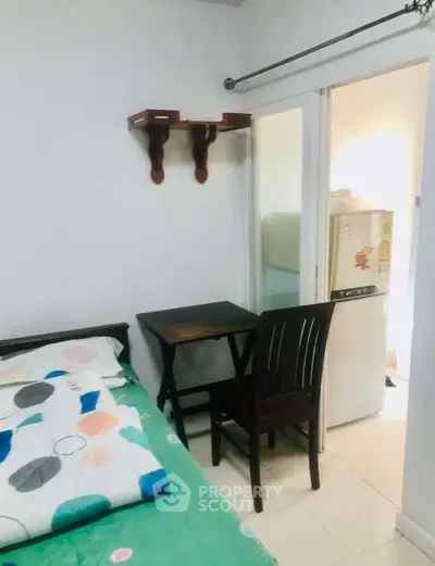 Cozy bedroom with a small desk and chair, adjacent to a compact kitchen area.