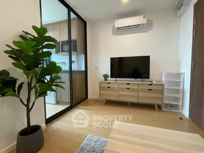 Modern living room with wooden flooring, TV unit, and sliding glass door to kitchen.