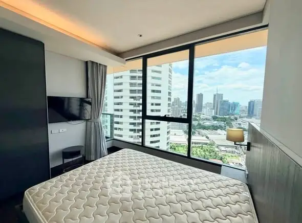 Modern bedroom with city view in high-rise apartment, featuring large windows and sleek design.