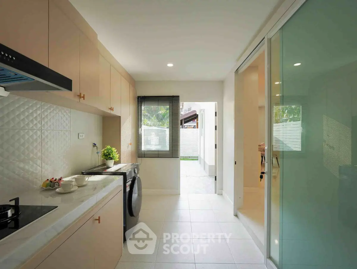 Modern kitchen with sleek cabinetry and glass sliding door, featuring a gas stove and washing machine.