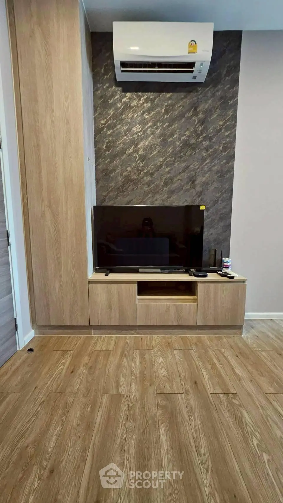 Modern living room with sleek wooden flooring and stylish TV setup under air conditioning unit.