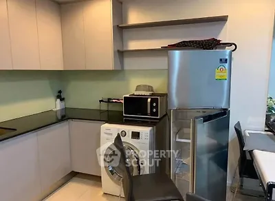 Modern kitchen with sleek cabinets, washing machine, and stainless steel fridge in a compact layout.