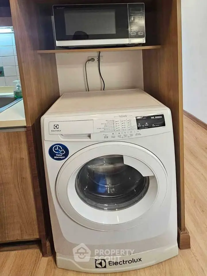 Modern laundry area with Electrolux washing machine and microwave in stylish wooden cabinet.