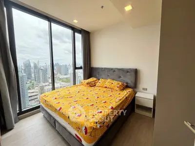 Modern bedroom with city view and large windows in high-rise apartment.