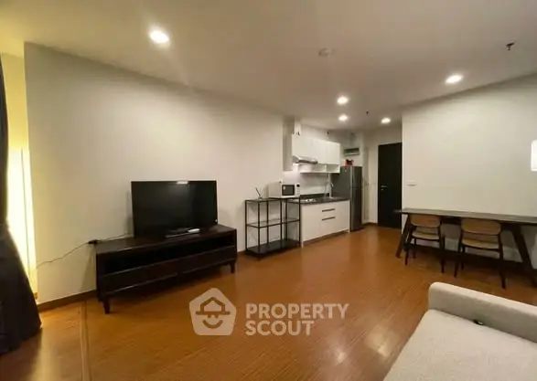 Modern living room with open kitchen and dining area, featuring sleek furniture and warm lighting.