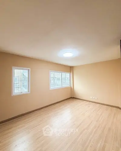 Spacious empty room with wooden flooring and ample natural light from two windows.